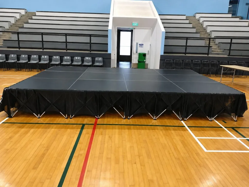 Modular platform stage with black skirting set up in a school sports hall in Singapore